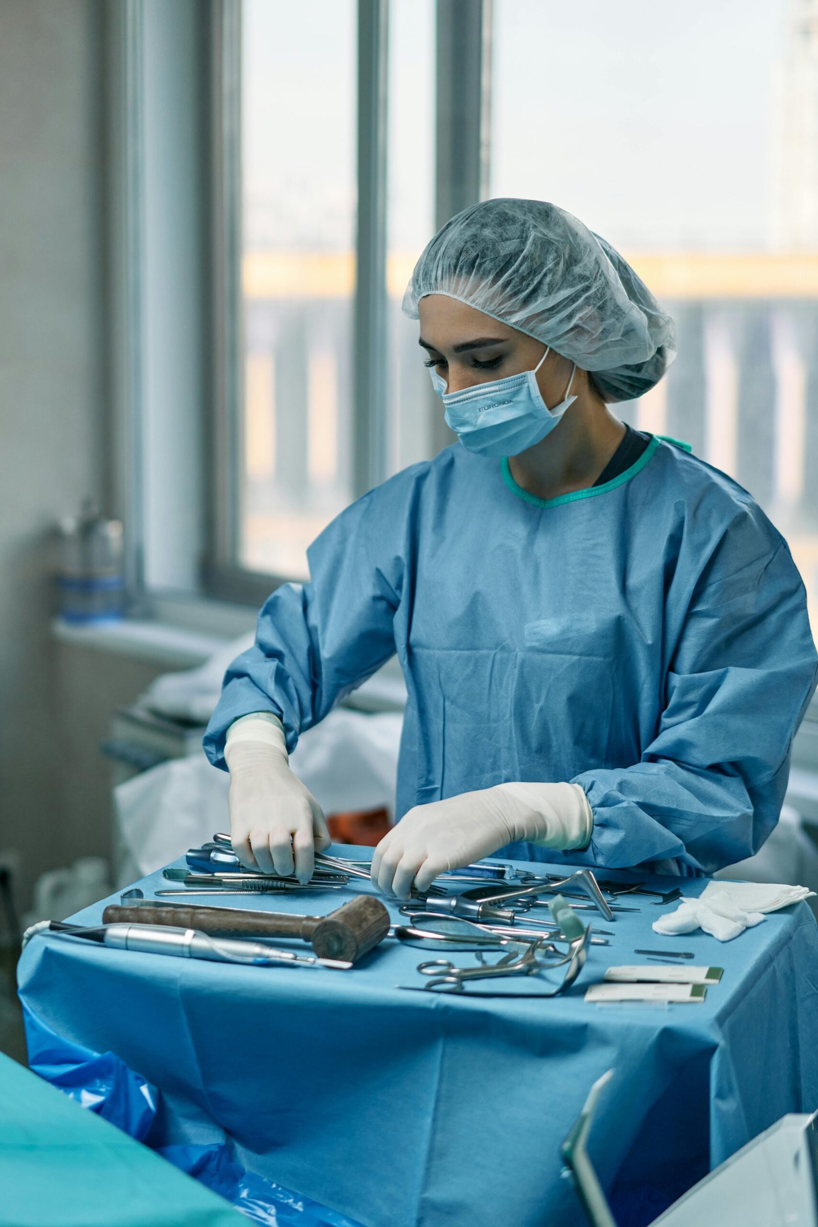A female surgeon wearing protective gear arranges surgical instruments in a hospital operating room.